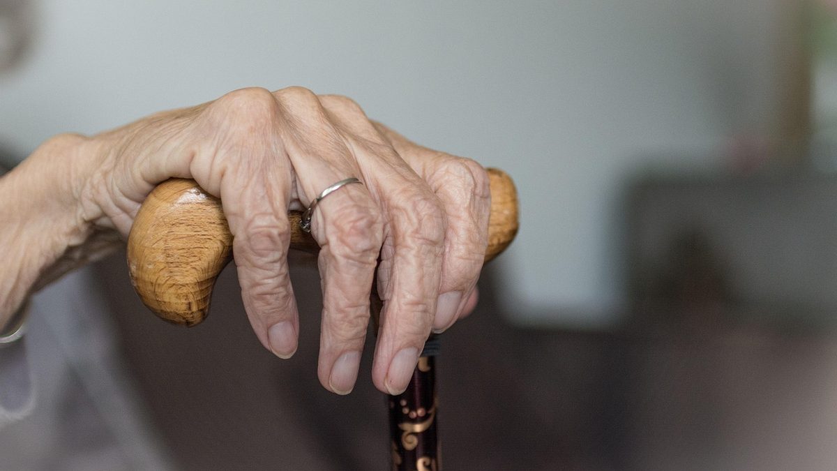 Mãos de pessoa idosa apoiadas em uma bengala