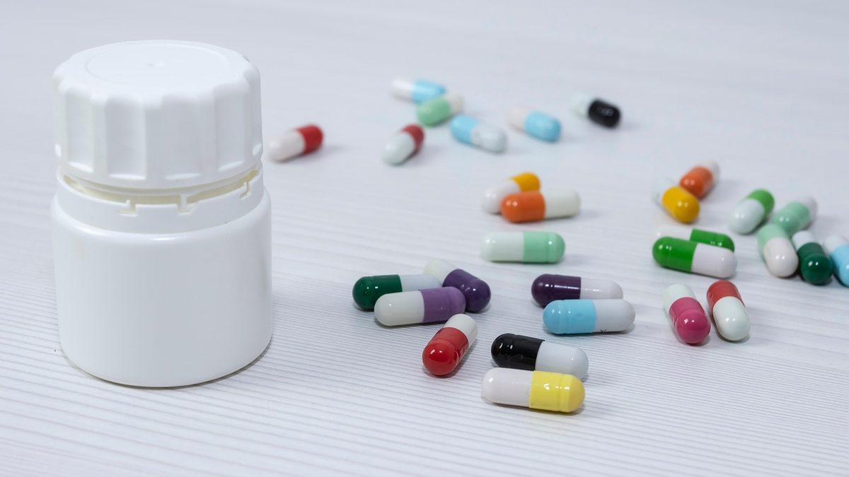 Frasco branco e cápsulas de medicamento sobre uma mesa