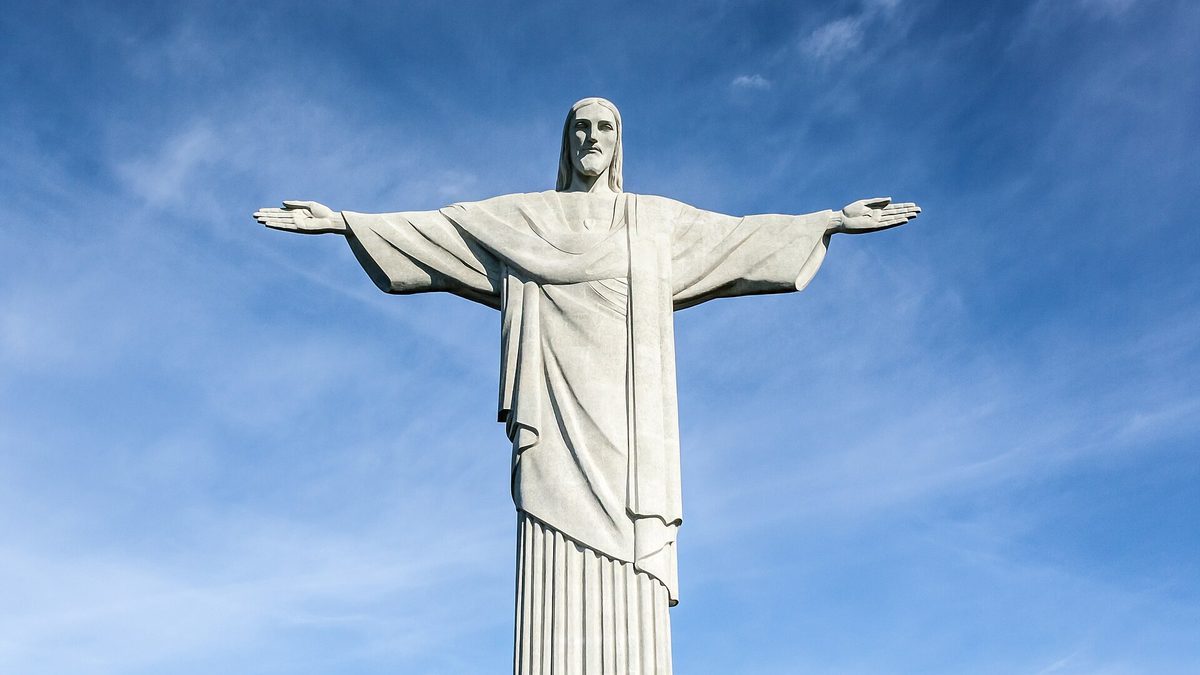 Estátua do Cristo Redentor de braços abertos sob céu azul, no Rio de Janeiro
